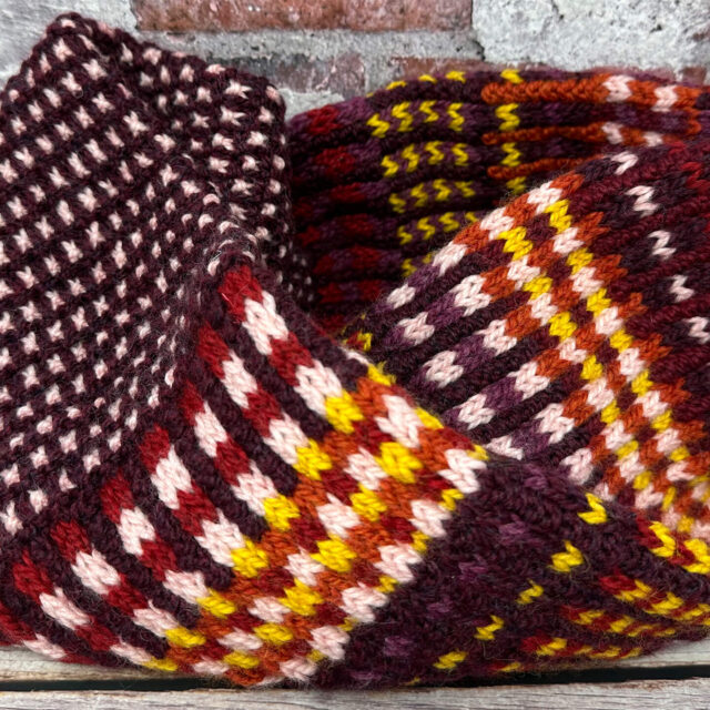 A photo of a hand knitted Black Mountain Cowl in from of a brick wall.